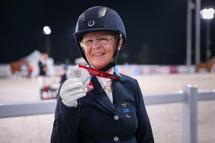 A female athlete holds a silver medal and smiles