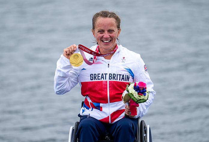 A female athlete sits on a wheelchair and holds a gold medal with her right hand.