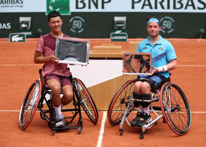 Two male wheelchair tennis players pose for a photo with their trophies.