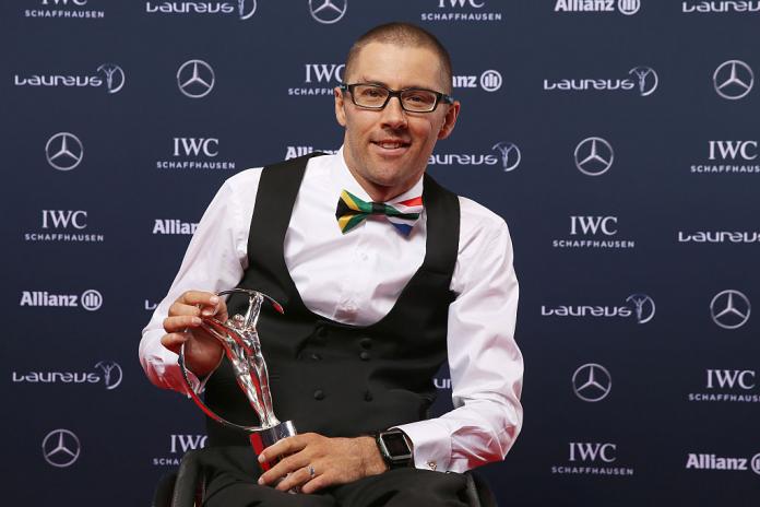 A male athlete poses at an awards ceremony with a silver trophy.