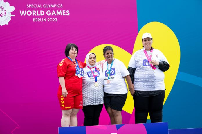 Four female athletes pose for a photo with their medals in front of the banner that reads "Special Olympics World Games Berlin 2023"