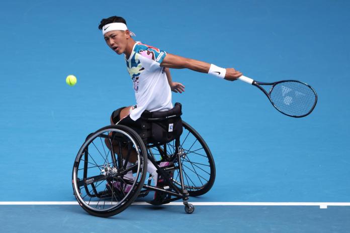 A male wheelchair tennis player hits a ball.