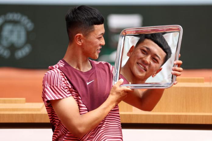 A male athlete holds the French Open trophy. His face is reflected on the silver trophy. 