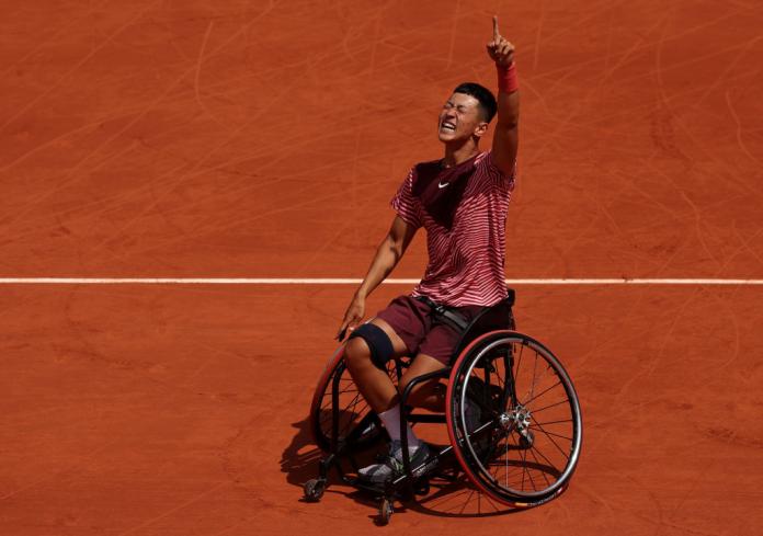 A male wheelchair tennis player raises his left arm.