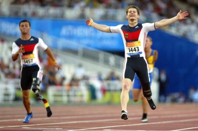 A male runner with a prosthetic leg celebrates with his arms wide open as he finished a race.