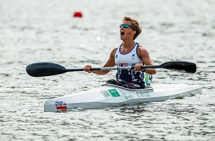 A female Para canoe athlete holds a paddle with both hands and celebrates on her boat.
