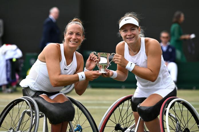 Two female wheelchair tennis players hold a trophy