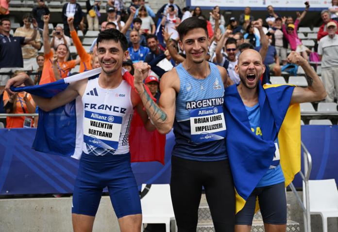 three male Para athletes holding up their flags and smiling in front of the fans