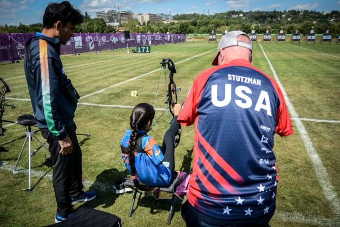 A male archer helps a female archer position her bow