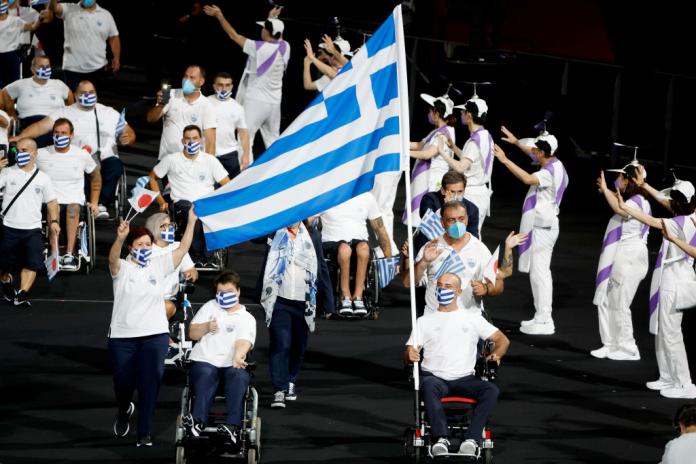 Dva sportovci na invalidním vozíku nesoucí vlajku Řecka v průvodu
