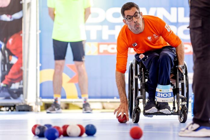 A male athlete grabs a red boccia ball during competition