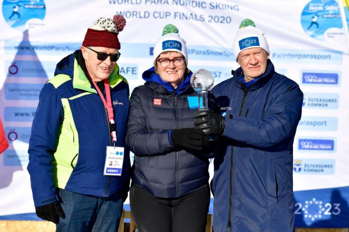 two men and a woman standing on a podium holding a crystal trophy