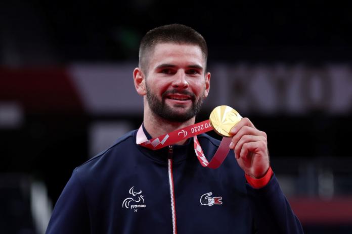A male athlete smiles while holding a gold medal