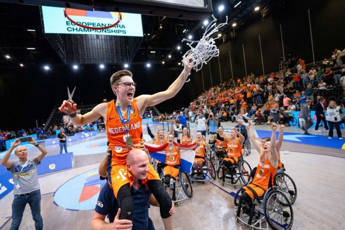 Tekerlekli sandalyeli bir basketbolcu basketbol ağını kesiyor, takım arkadaşları kutlama yapıyor