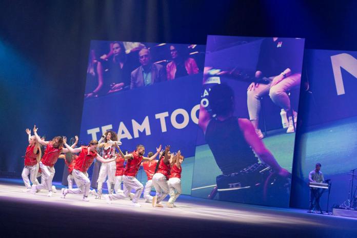 A group of dancers in red and white costumes moving on stage