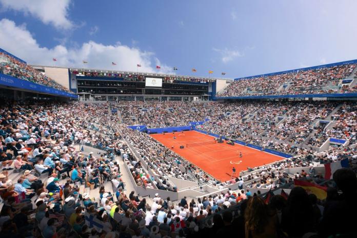 a wide shot of a clay tennis court surrounded by spectators 