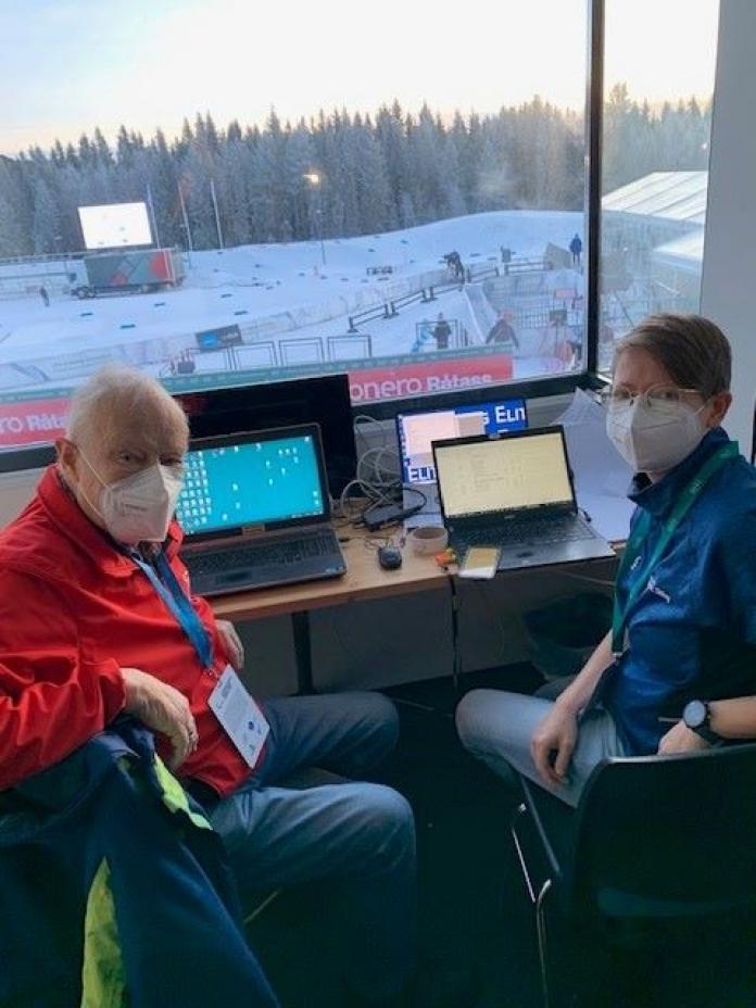 a man and a woman in masks sitting at computers overlooking a ski slope