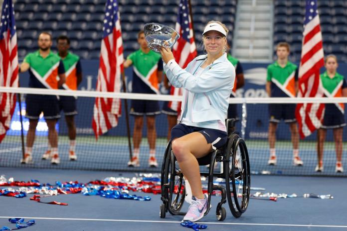 A female wheelchair tennis player lifts a trophy