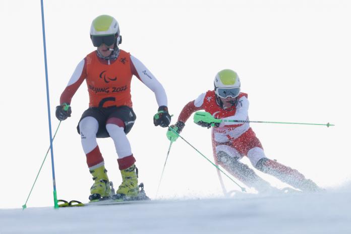 A male sighted guide skis in front of a male Para athlete.