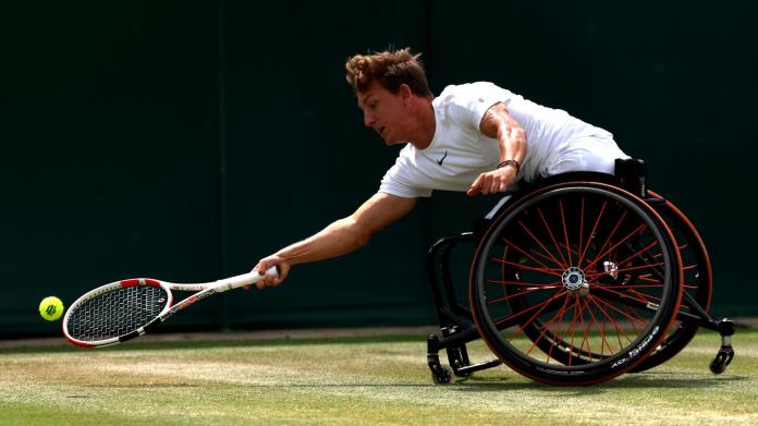 A male wheelchair tennis player reaches out for a ball during a match.