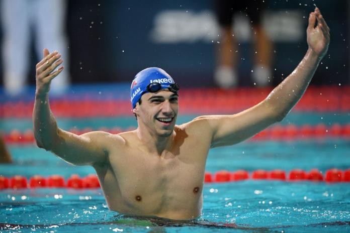A male swimmer raises both hands in the pool to celebrate his victory.