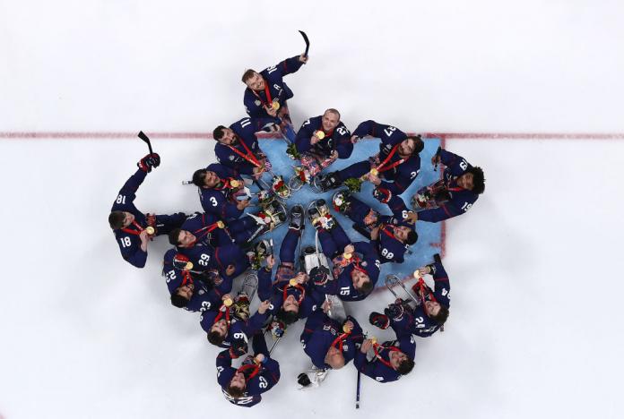 Team USA Para ice hockey players celebrate after receiving their gold medals. The photo is taken from above and the players are looking up at the camera.