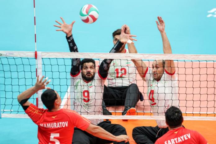 Two male athlete try to block a ball, while two others try to spike it.