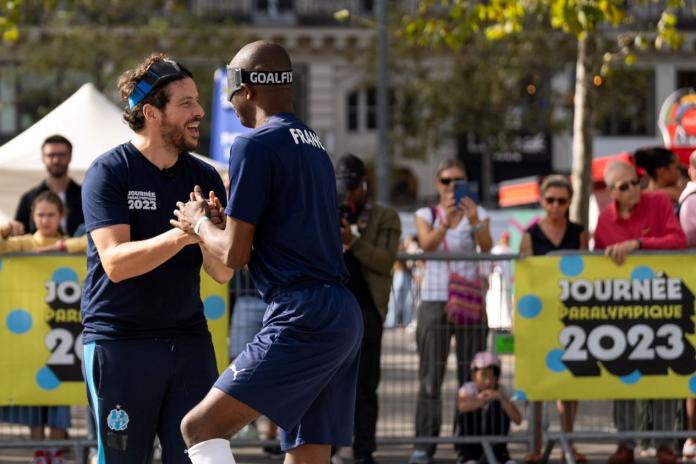 Two male athletes hold hands as a crowd watches them