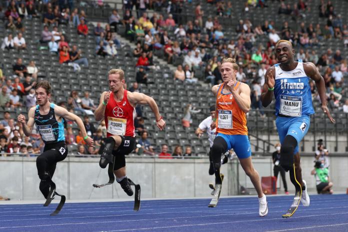 Four male athletes using running blades race. People are watching from the stands.
