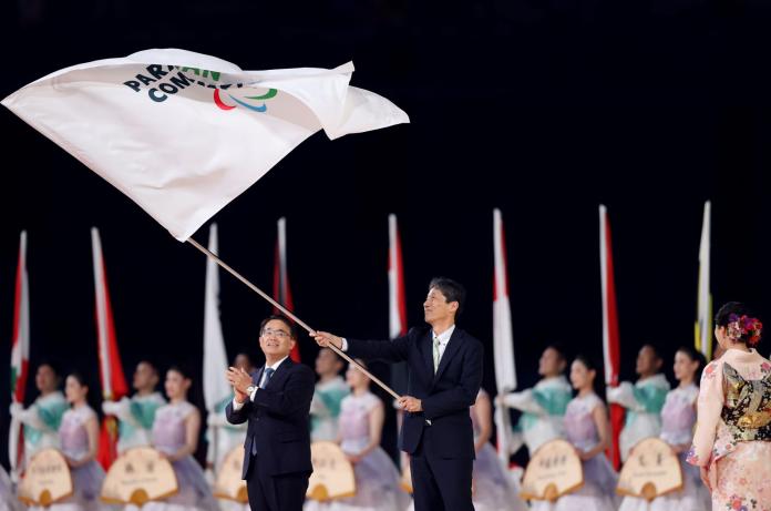 A male official wearing a suit waves the flag of the Asian Paralympic Committee during the closing ceremony of the Hangzhou 2022 Asian Para Games.