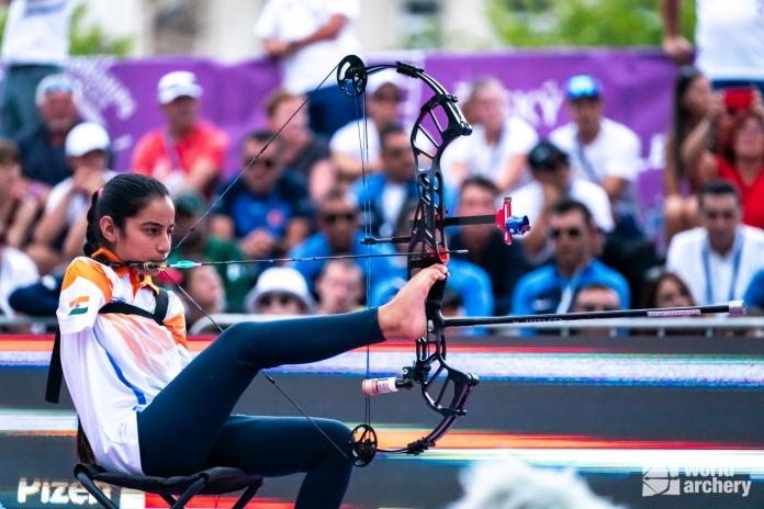 A female athlete without arms aims her shot by holding the bow with her right leg.