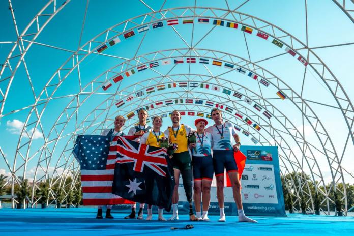 Six athletes, or three pairs of male and female athletes - pose for a photograph after receiving medals at the World Rowing Championships. The athletes in the center are holding an Australian flag.
