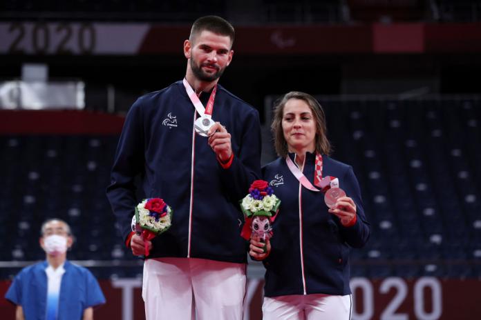 A male and a female athlete pose for a photo on the podium at the Tokyo 2020 Paralympics. They are holding silver medals and bouquets