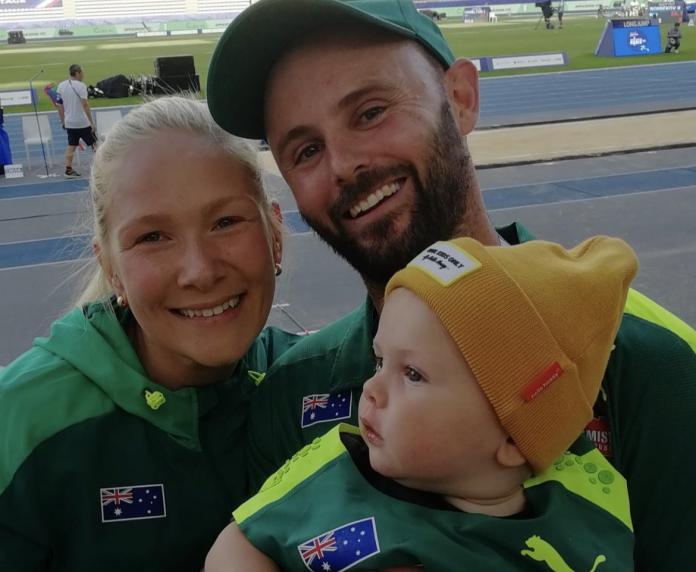 A family portrait. A female athlete, her husband, and their son posing for a photograph. They are all wearing Australia's green and gold track suit.