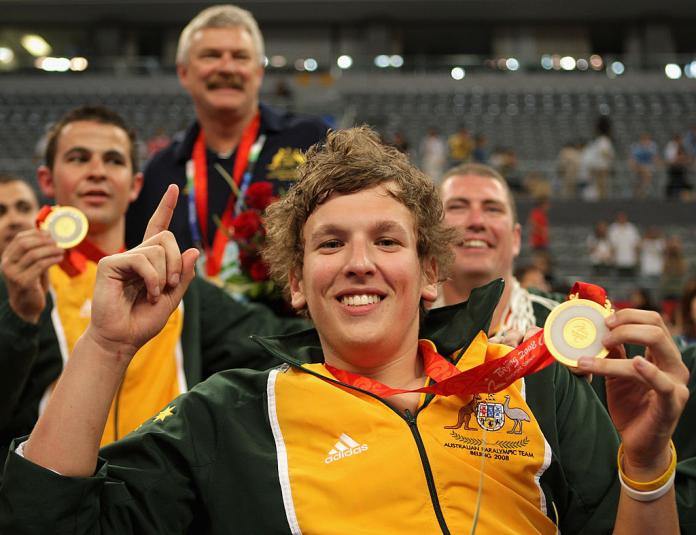 Four male wheelchair basketball players and staff celebrate after winning a gold medal