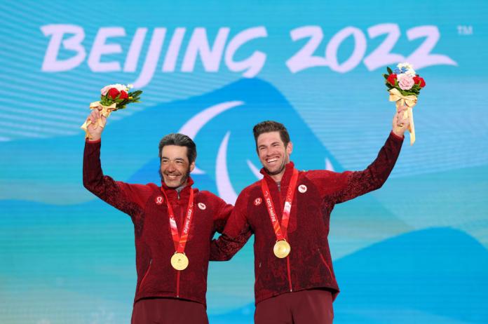 Two male athletes pose for a photo with their gold medals.