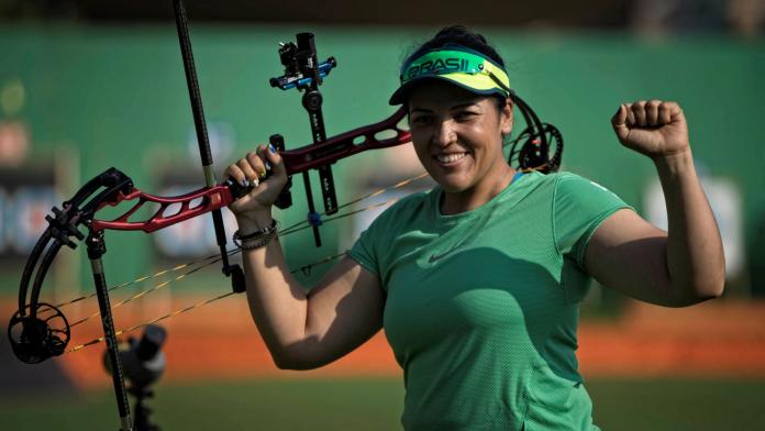 A female Para archer holds a bow with her right hand and pumps her left fist.