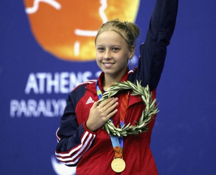 A young female athlete waves her left hand after receiving a gold medal.