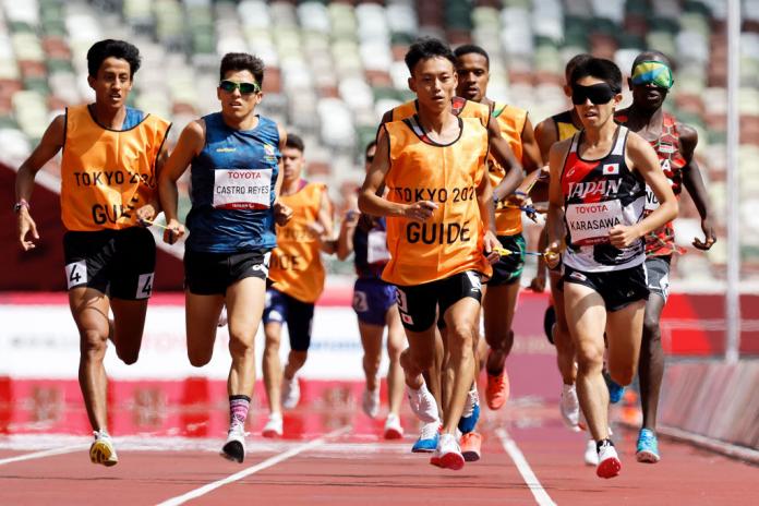 Male athletes wearing eye shades and their sighted guides run on the track