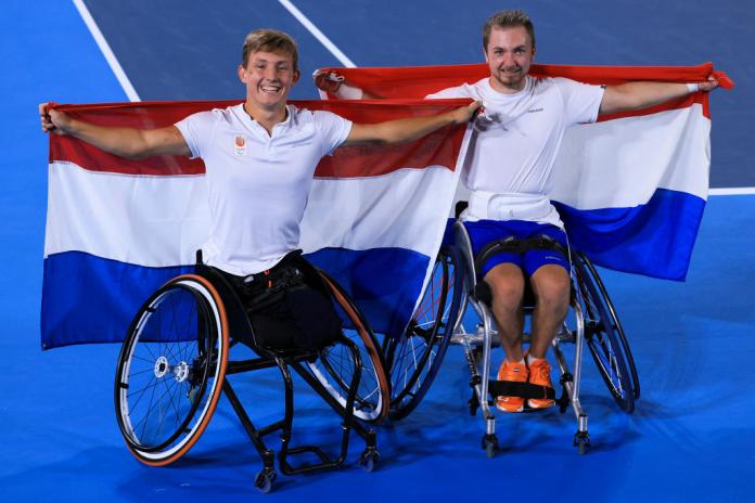 Two male wheelchair tennis players celebrate by raising the Dutch flag
