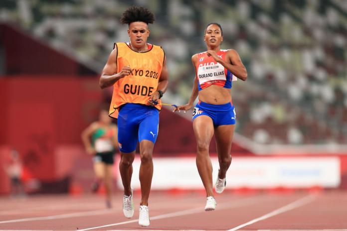 A female sprinter and her male guide are racing at Tokyo 2020. They are holding a tether.