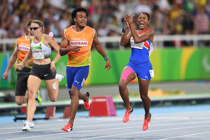 A female sprinter claps her hands on the track after winning a race. Her male guide is next to her.