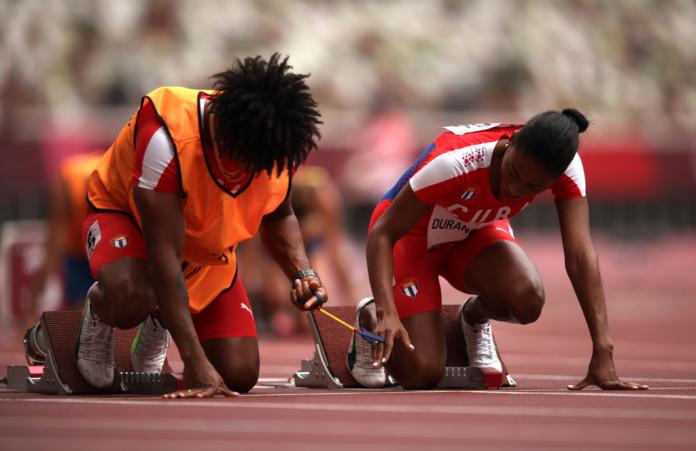 A close-up image of a female sprinter and her guide on the starting blocks. They hold a tether.