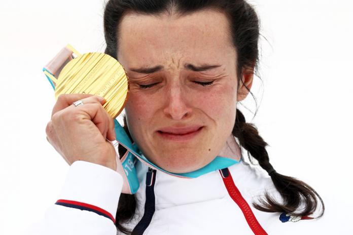 A close-up photo of a female Para athlete holding a gold medal in front of her face. Her eyes are closed.