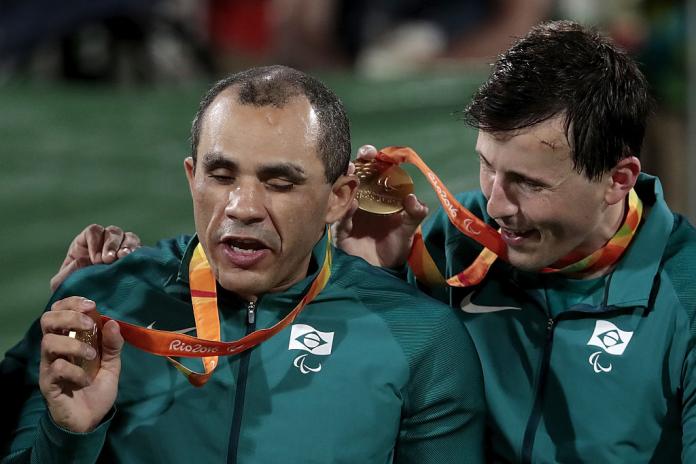 One male athlete shakes a gold medal for his teammate to hear.