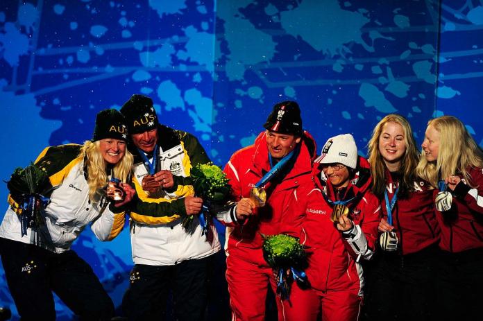 Three female skiers and their guides pose on the podium.