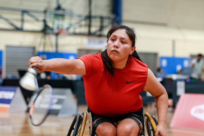 A female Para badminton player, who competes in a wheelchair, holds a racquet and smiles