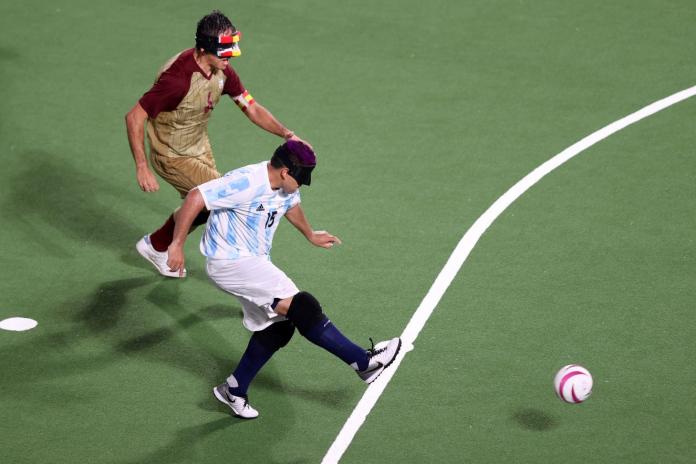 A male blind football player kicks the ball with his left foot