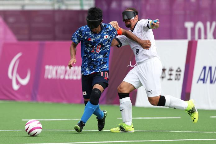 A male blind football player dribbles the ball past an opponent.