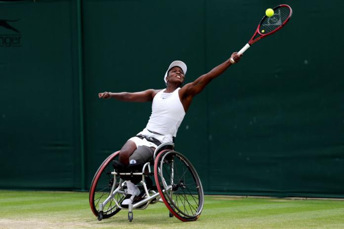 A female wheelchair tennis player stretches to play a forehand during a match.